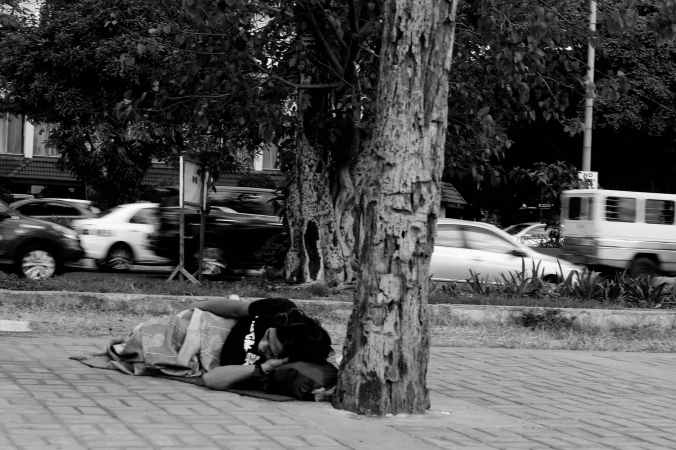 grayscale photo of man lying beside tree